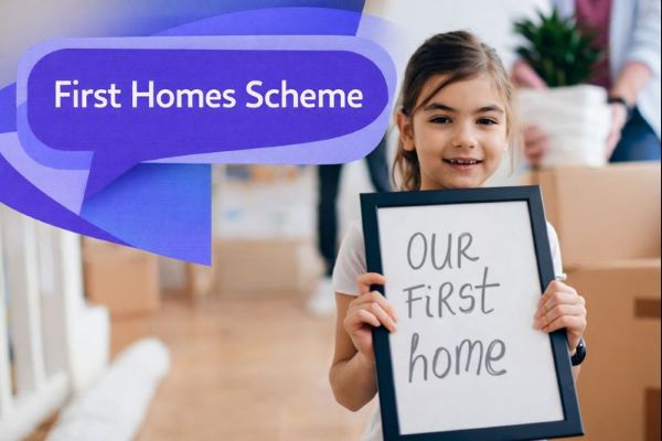 First Homes Scheme graphic showing a smiling child holding a framed sign in a new home with moving boxes in the background, alongside a unique dark blue and light blue speech bubble containing Open Sans text “First Homes Scheme”.