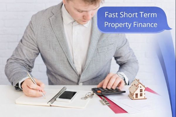 Bridging Loans | A man in a light grey blazer sits at a white desk calculating figures and writing notes, with a calculator, keys, and a small wooden house model beside him. On the right side, curved blue Connect Mortgages brand shapes frame a blue speech bubble in Open Sans reading “Fast Short Term Property Finance.”
