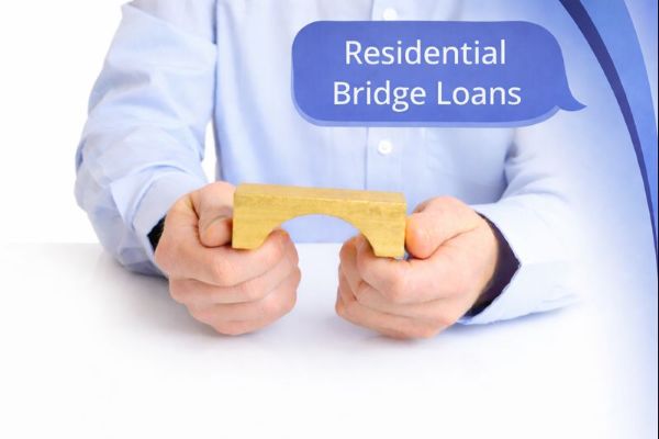 A close-up image of a person wearing a light blue shirt holding a small wooden bridge model in both hands on a white surface. A blue speech bubble in the top-right corner reads “Residential Bridge Loans,” with curved blue brand accents framing the design.