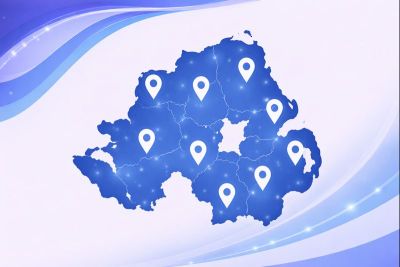 Vector map of Northern Ireland in light and dark blue branding colours, showing the country outline with internal county boundaries and multiple location pin icons placed across the map to indicate service coverage areas.
