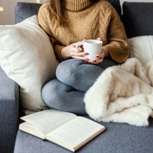 Person relaxing on a sofa with a blanket, holding a mug and reading a book at home, reflecting on remortgage options in a calm and comfortable living room setting.
